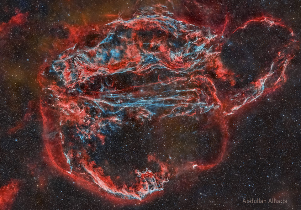The featured image shows a night sky with a large complex nebula in red and blue. The Veil Nebula has several famous components such as the Bat and Witch's Broom Nebulas. Please see the explanation for more detailed information.