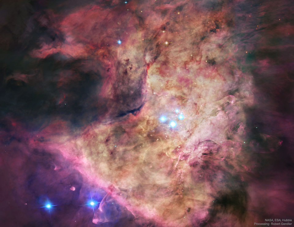 A bright nebula occupies the center of the frame. The nebula is complex but roughly tan in the center and red around the edges. In the center are four bright blue stars. Please see the explanation for more detailed information.