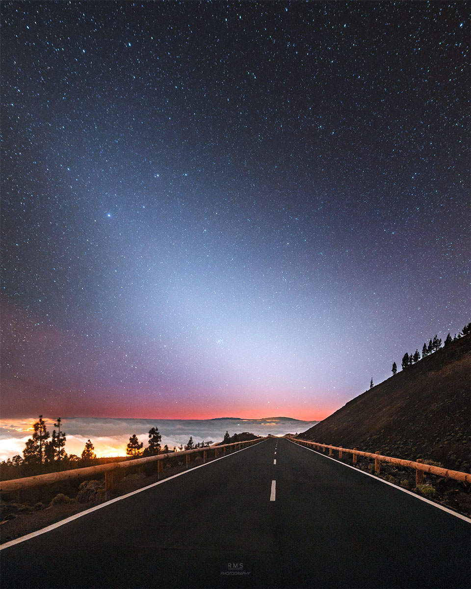 A night sky is shown above a road going off into the distance. An unusual area of brightened sky that does not block background stars appears diagonally from the lower right across the sky. Please see the explanation for more detailed information.